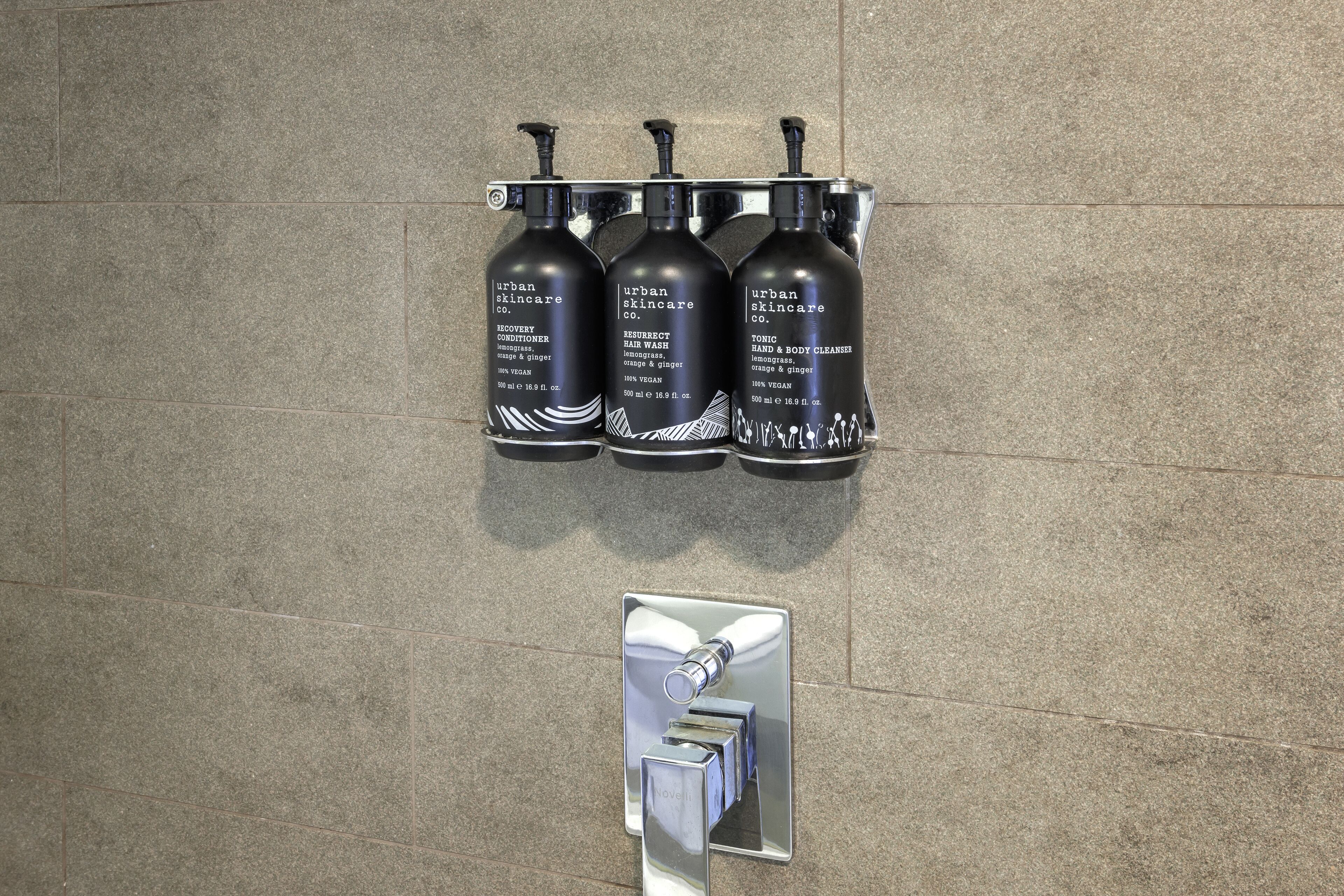 Tres botellas negras de productos Urban Skincare en un dispensador fijado a la pared.