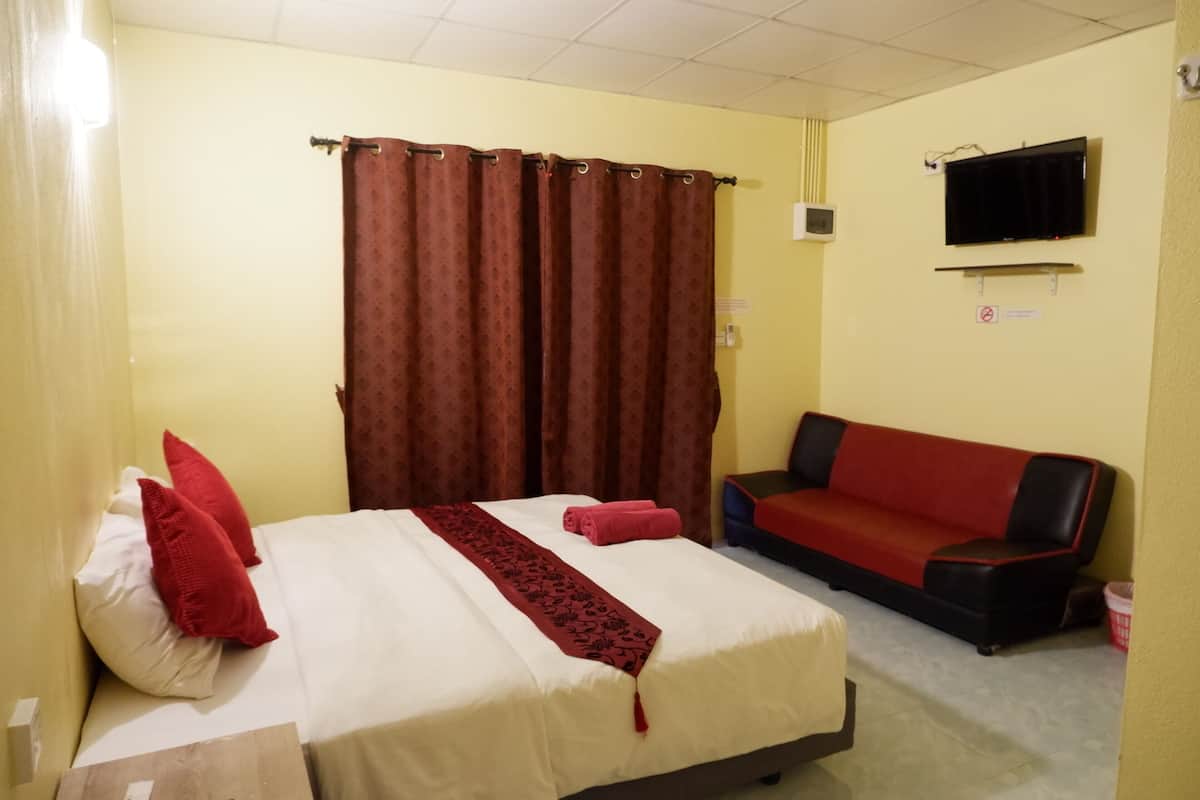 A hotel room with a bed, a red and black sofa, a TV mounted on the wall, and a curtain.