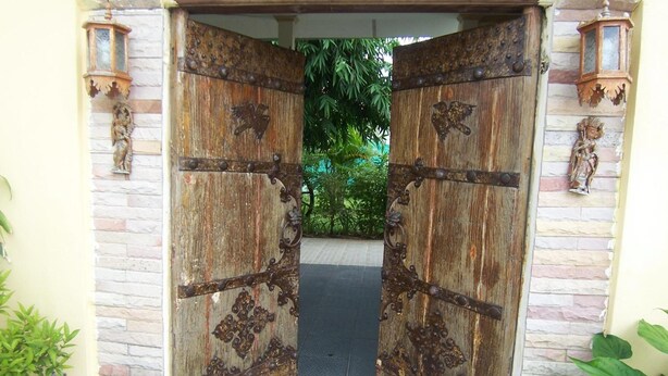 Une porte en bois rustique, agrémentée d’éléments décoratifs en métal, et un mur de pierres de chaque côté.
