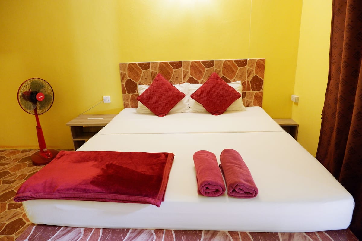 A hotel room with a bed, two red pillows, a red blanket, and two rolled towels.