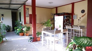 Une terrasse couverte avec une table et des chaises, entourée de plantes en pot.