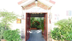 Une porte d’entrée avec une pancarte indiquant le comptoir d’enregistrement, des plantes en pot et un sol carrelé menant à un bâtiment.