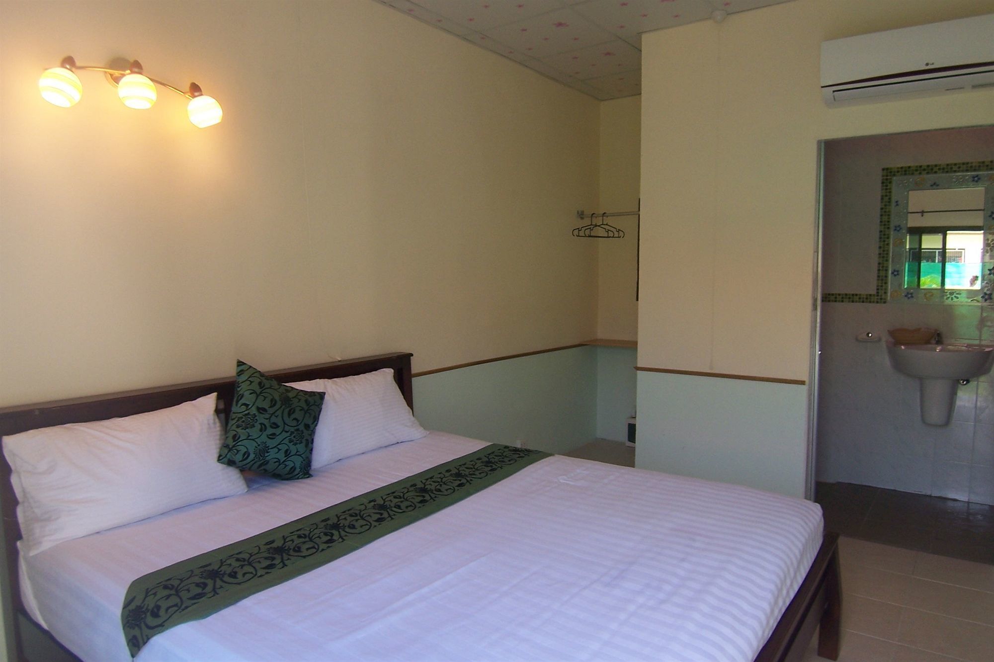 Una habitación de hotel con cama, mesita de noche, lámpara de pared, baño con lavamanos y espejo, y ducha.
