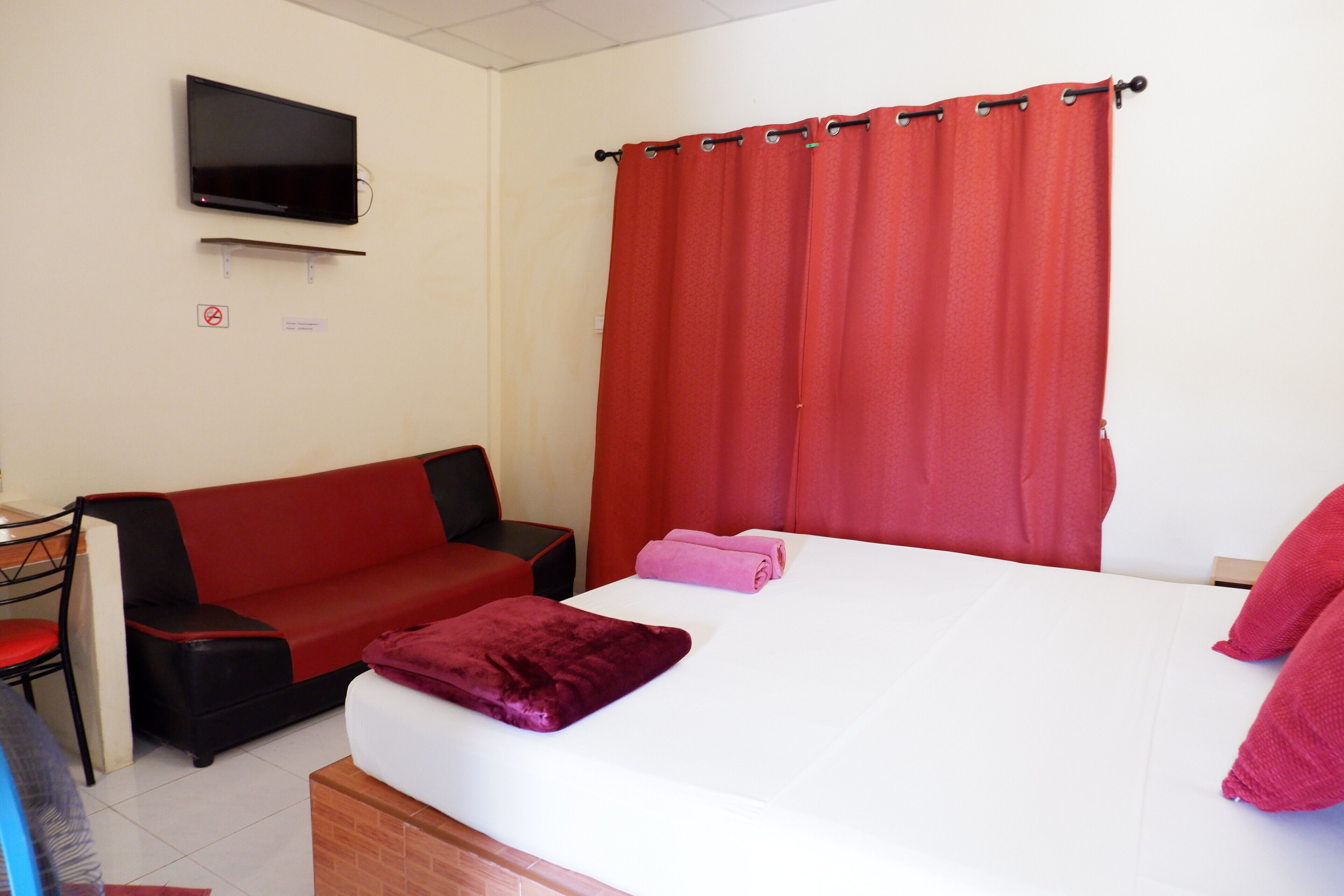 A hotel room with a bed, a red sofa, a TV mounted on the wall, and a curtain.