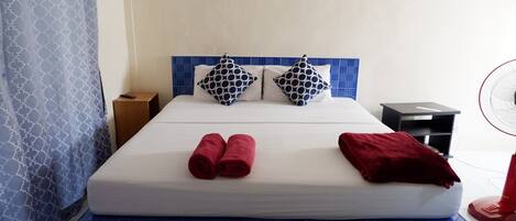 A hotel room with a bed, two pillows, a red blanket, and a red fan.