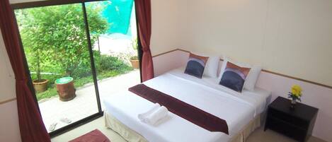 A bedroom with a large bed, a nightstand, a window with curtains, and a view of greenery outside.