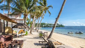 A beachside lounge with lounge chairs and tables, palm trees, and a view of the ocean. - Levantin (Boracay Island)
