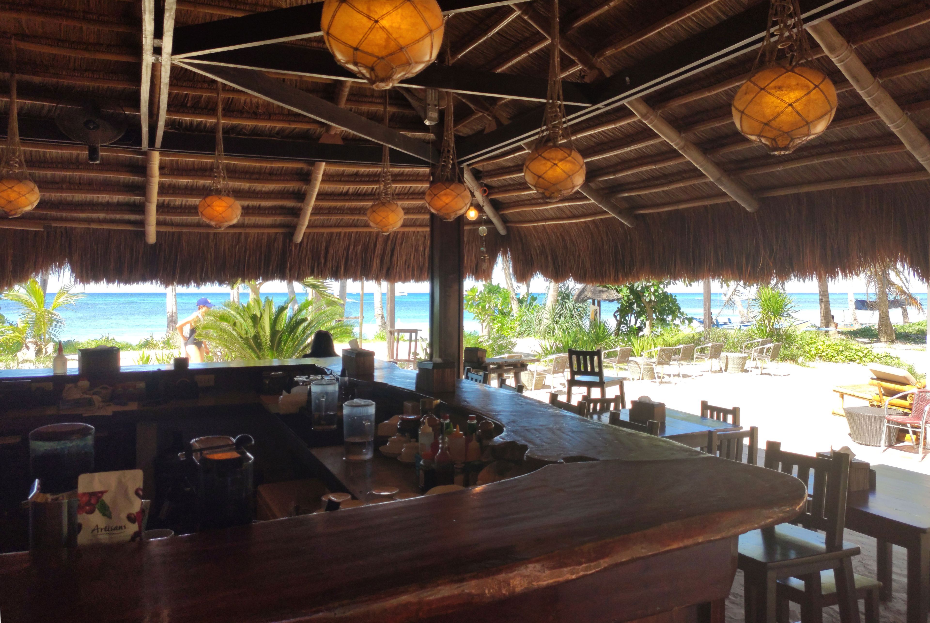 A beachside bar with a thatched roof, wooden furniture, and a view of the ocean.