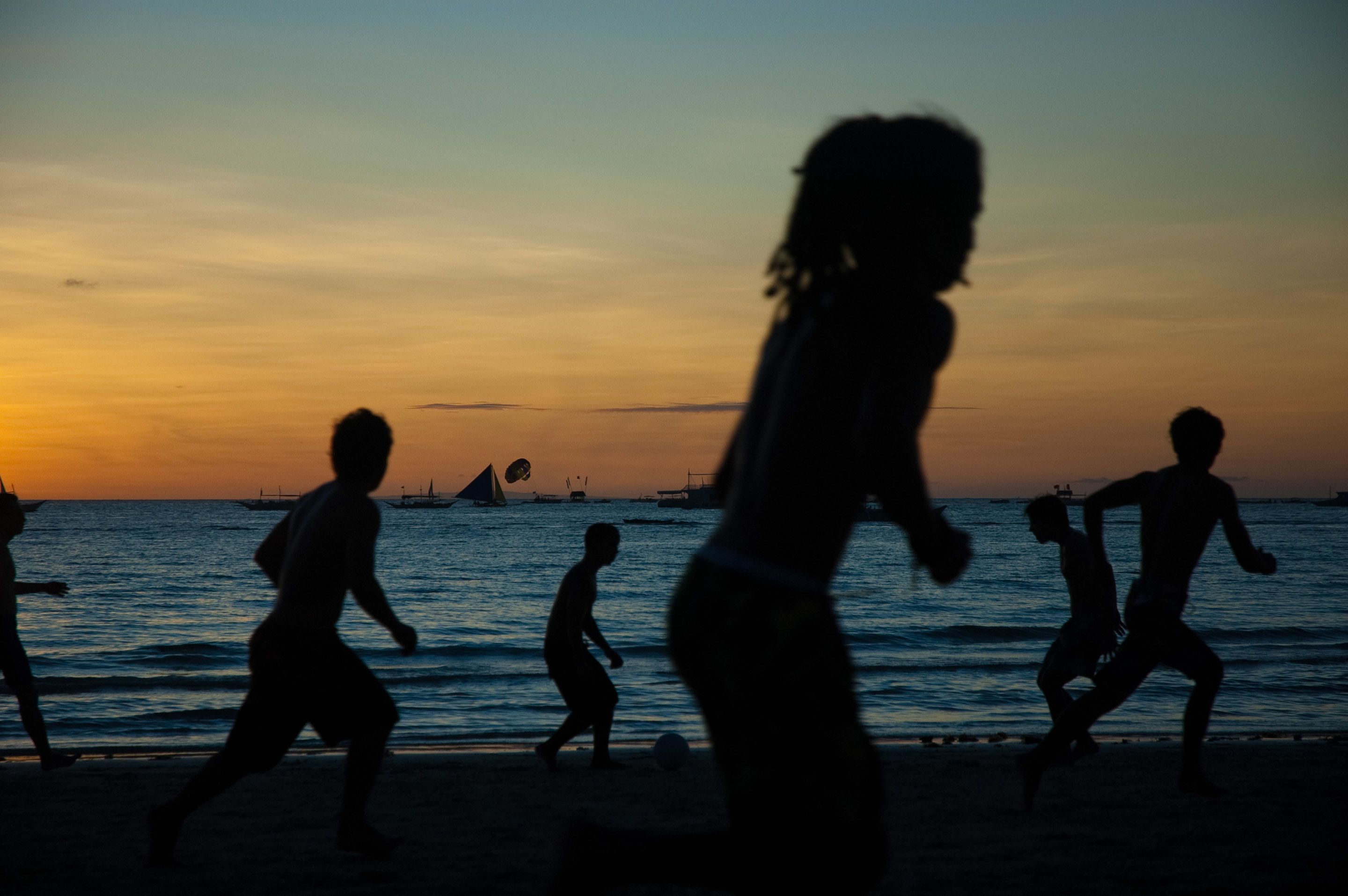Siluetes de persones jugant a futbol platja al capvespre.