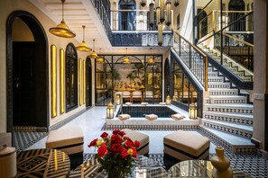 Un vestíbulo lujoso con una zona de estar central, piscina y una imponente escalera.