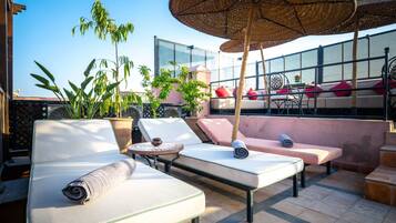 Een dakterras met loungezetels, een tafel en een grote parasol.