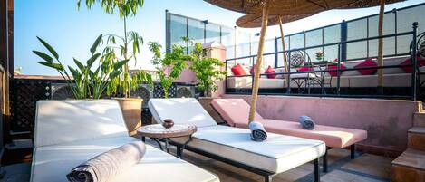 A rooftop lounge with lounge chairs, a table, and a large umbrella.