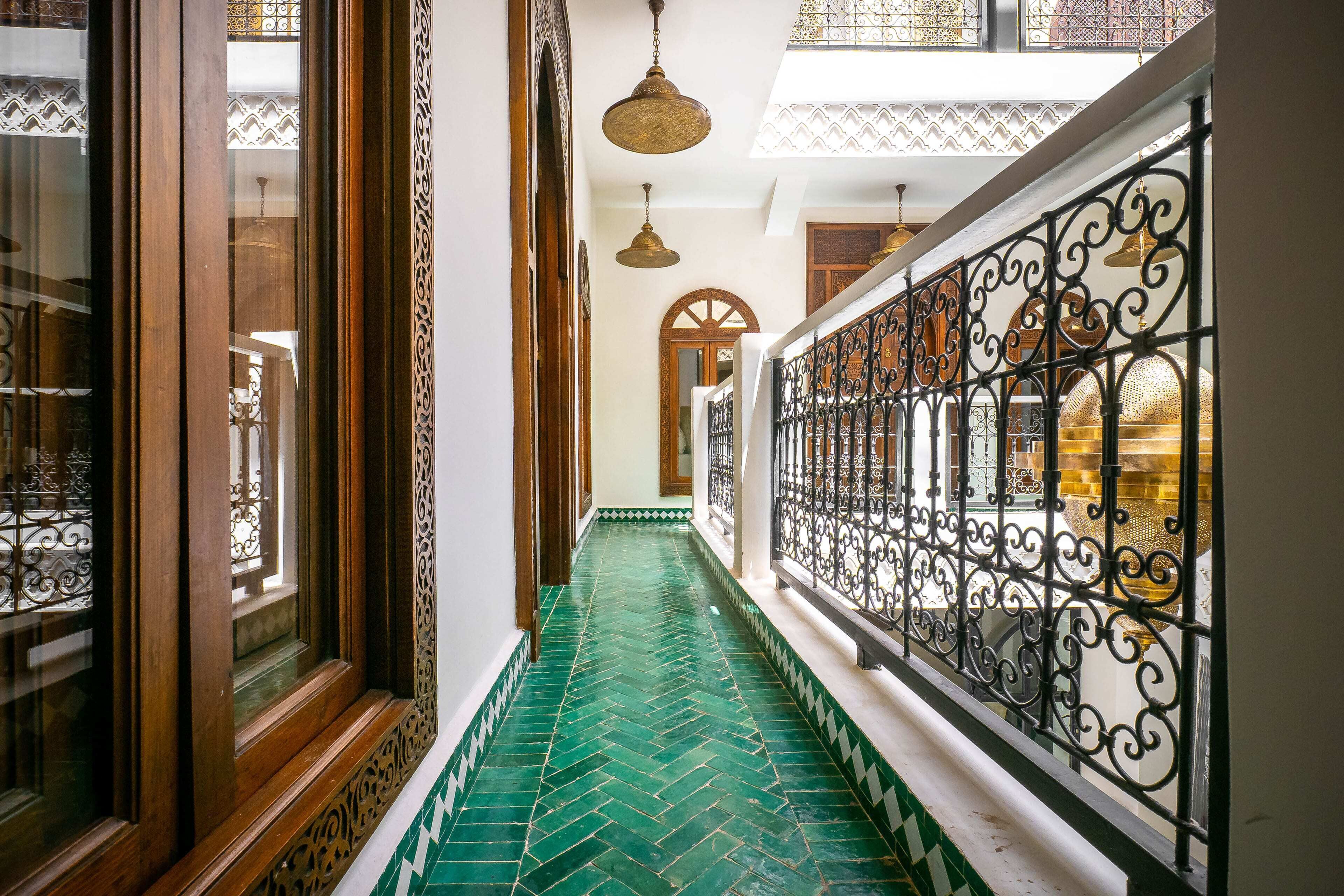 A corridor with patterned flooring, ornate metal railings, and a view of a room with a large, ornate door.