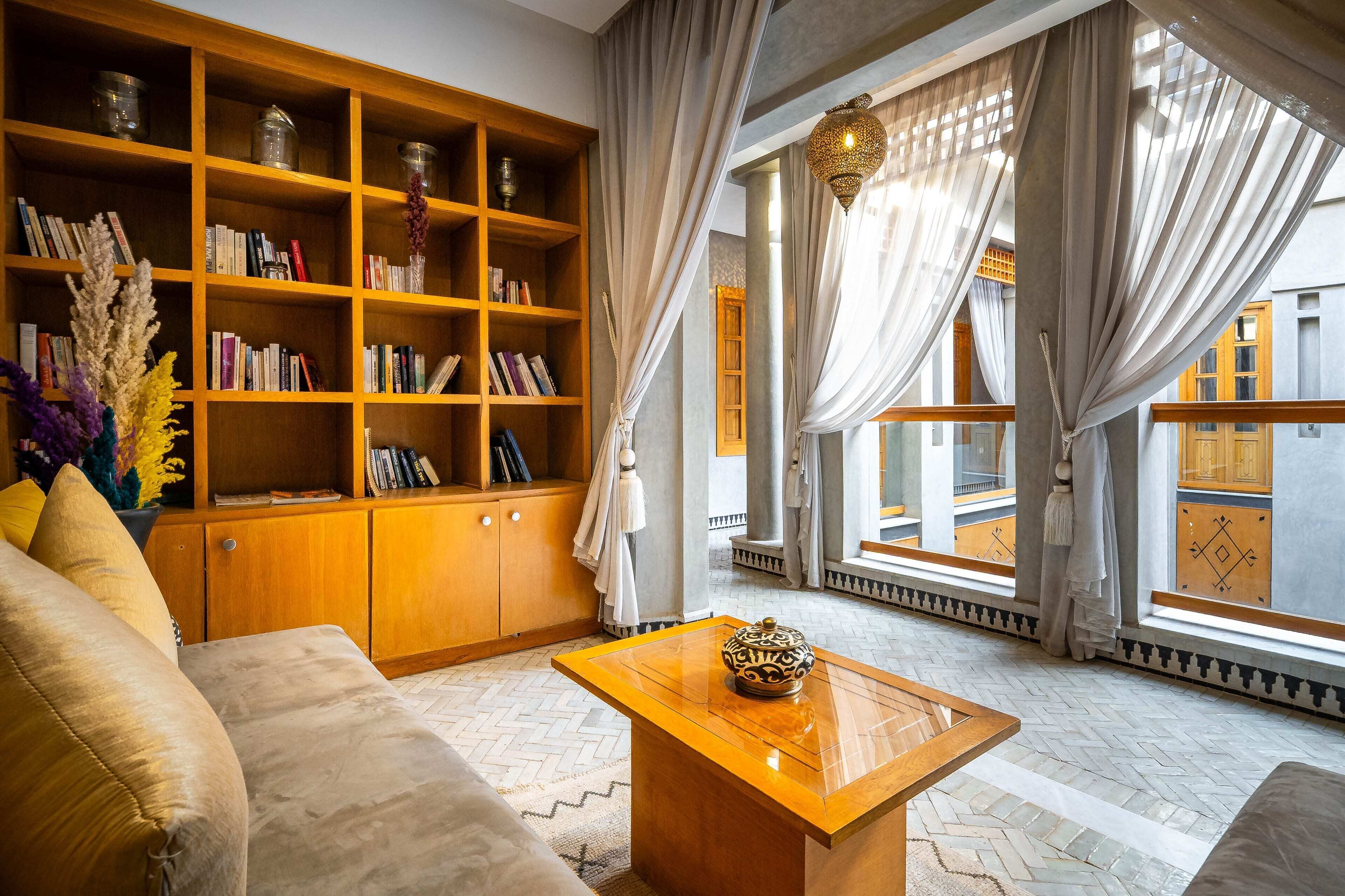 A living room with a sofa, a wooden bookshelf, a coffee table, and large windows with curtains.