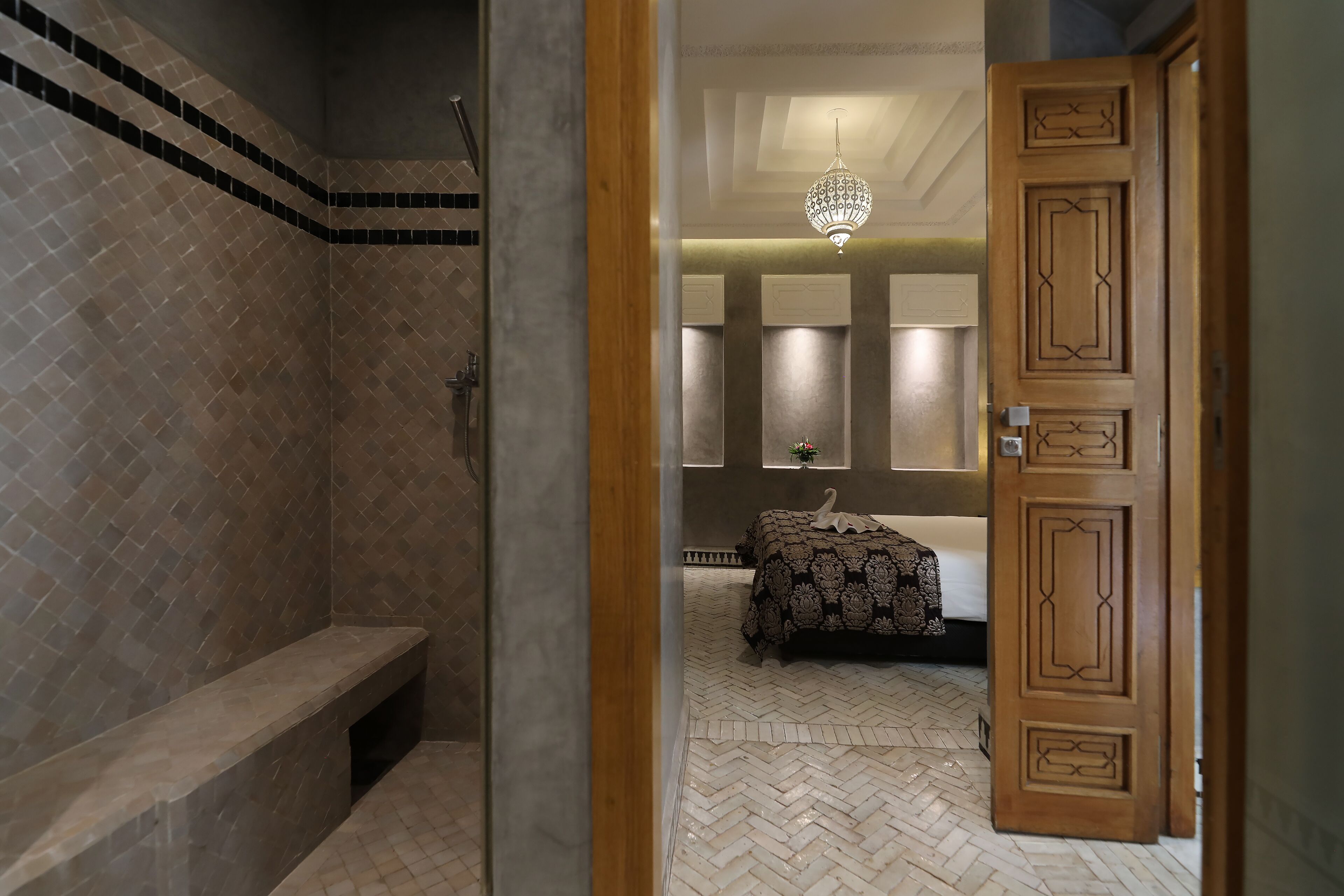A bathroom with a shower, bench, and a bed with a patterned bedspread.