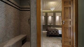 Un baño con ducha, asiento y cama con colcha estampada.