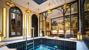 A luxurious indoor pool with a checkered tile pattern, elegant lighting fixtures, and a view of a dining area through large windows. - Riad L'Etoile D'Orient (Marrakech)