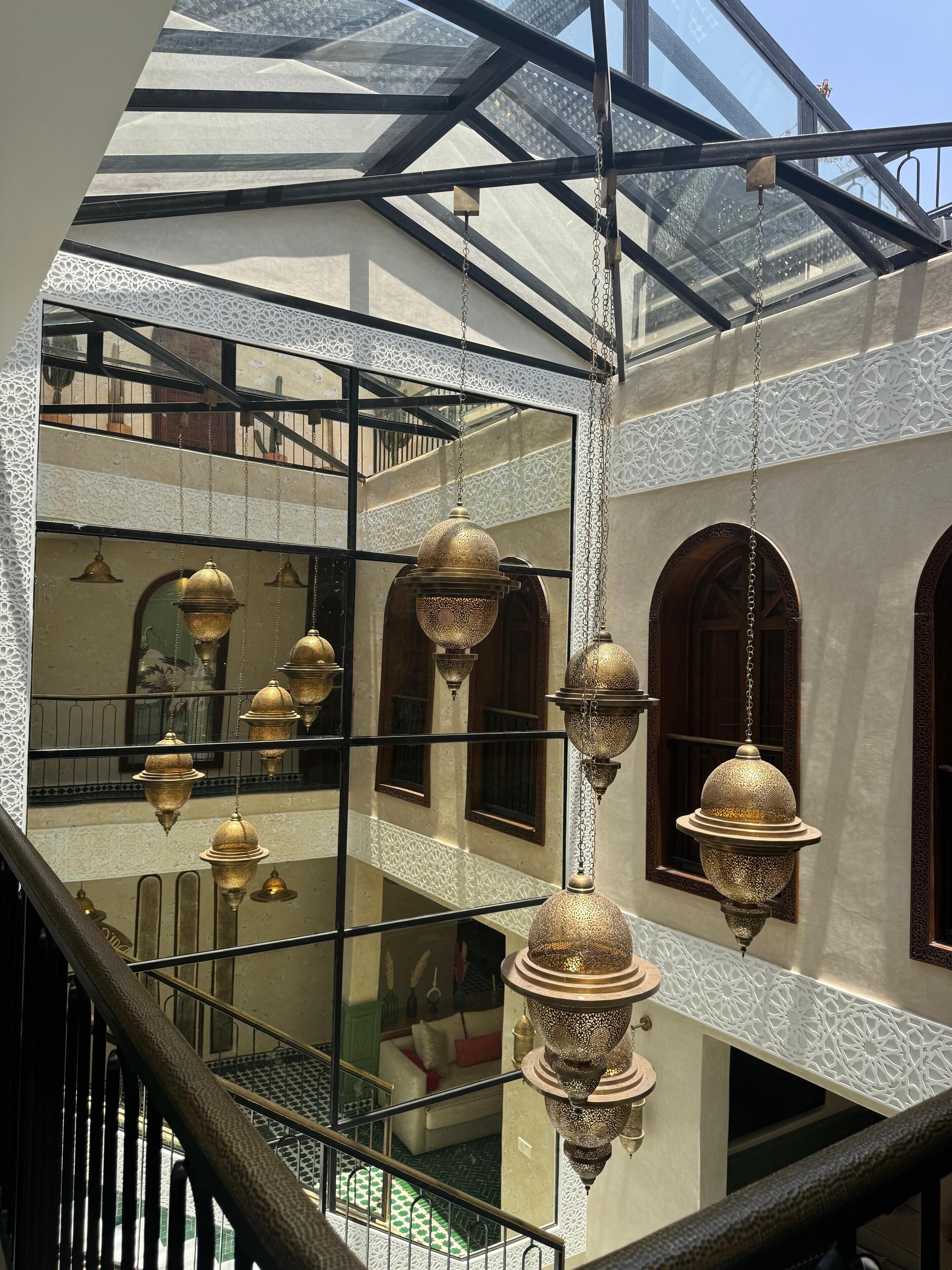 A multi-level atrium with ornate hanging lamps, a glass ceiling, and a staircase.