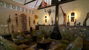 A cozy lounge area with plush green sofas, a stone fireplace, and various decorative items including a giraffe sculpture and wall-mounted lights.
