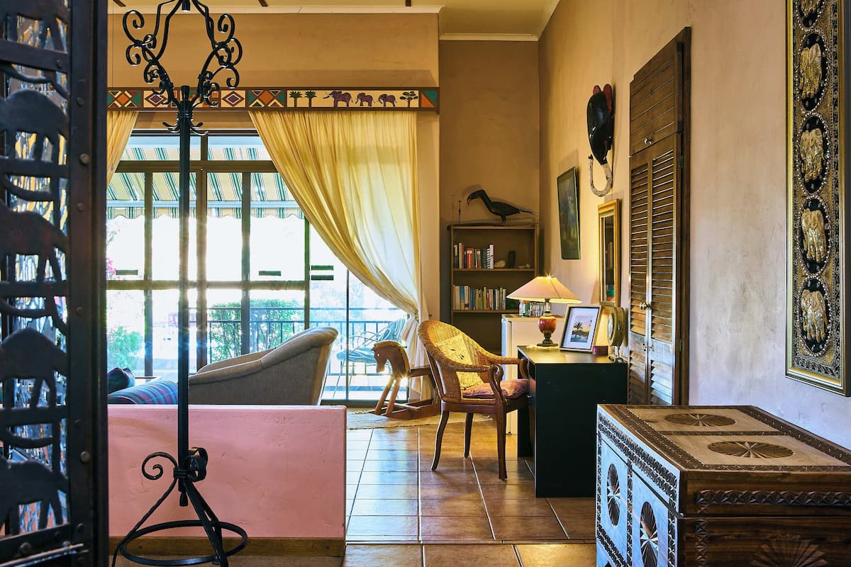 A room with a bed, a chair, a desk with a lamp, a bookshelf, and a window with curtains.