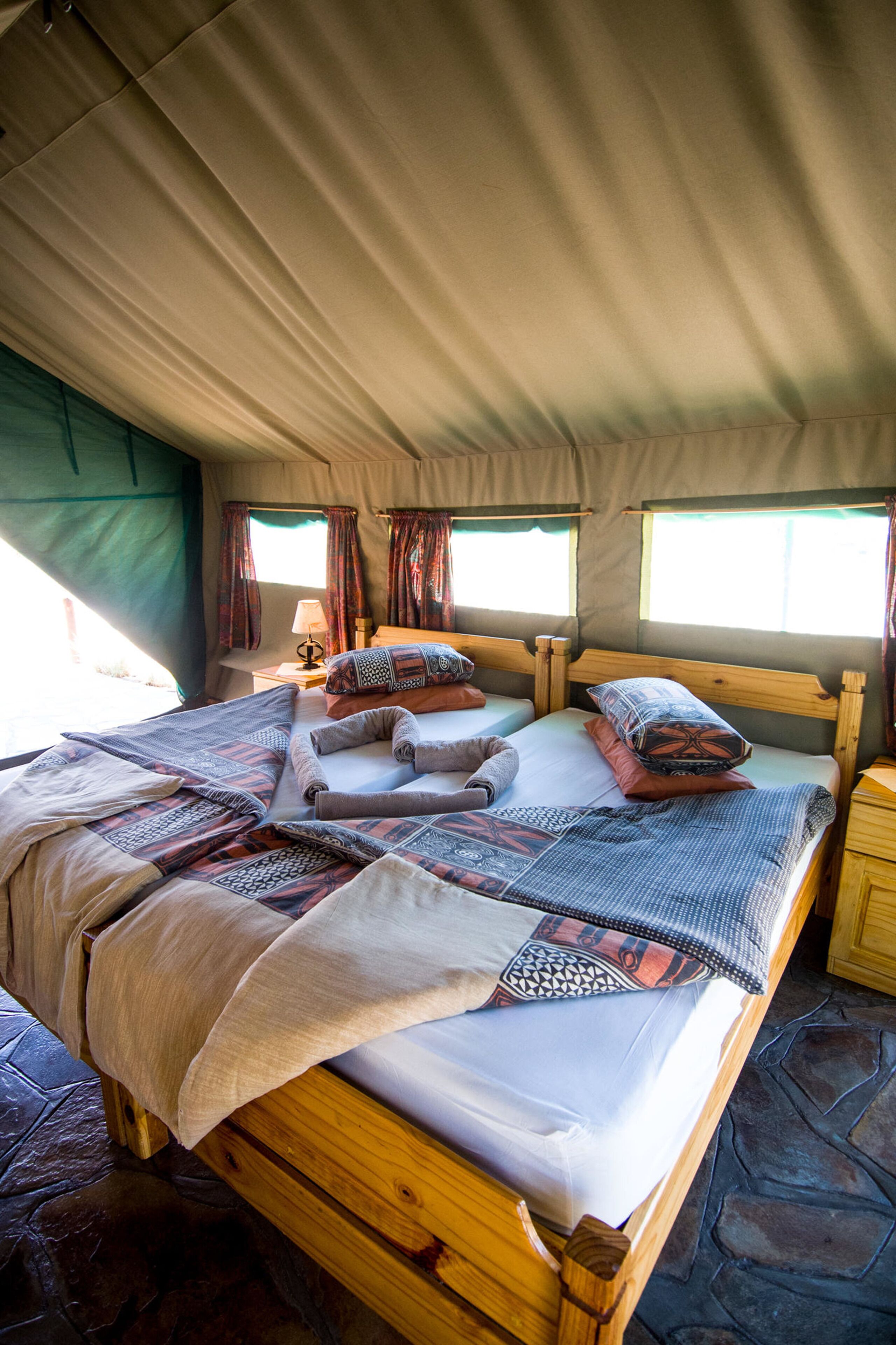 Een tentaccommodatie met twee houten bedden, elk voorzien van beddengoed en kussens met een patroon.