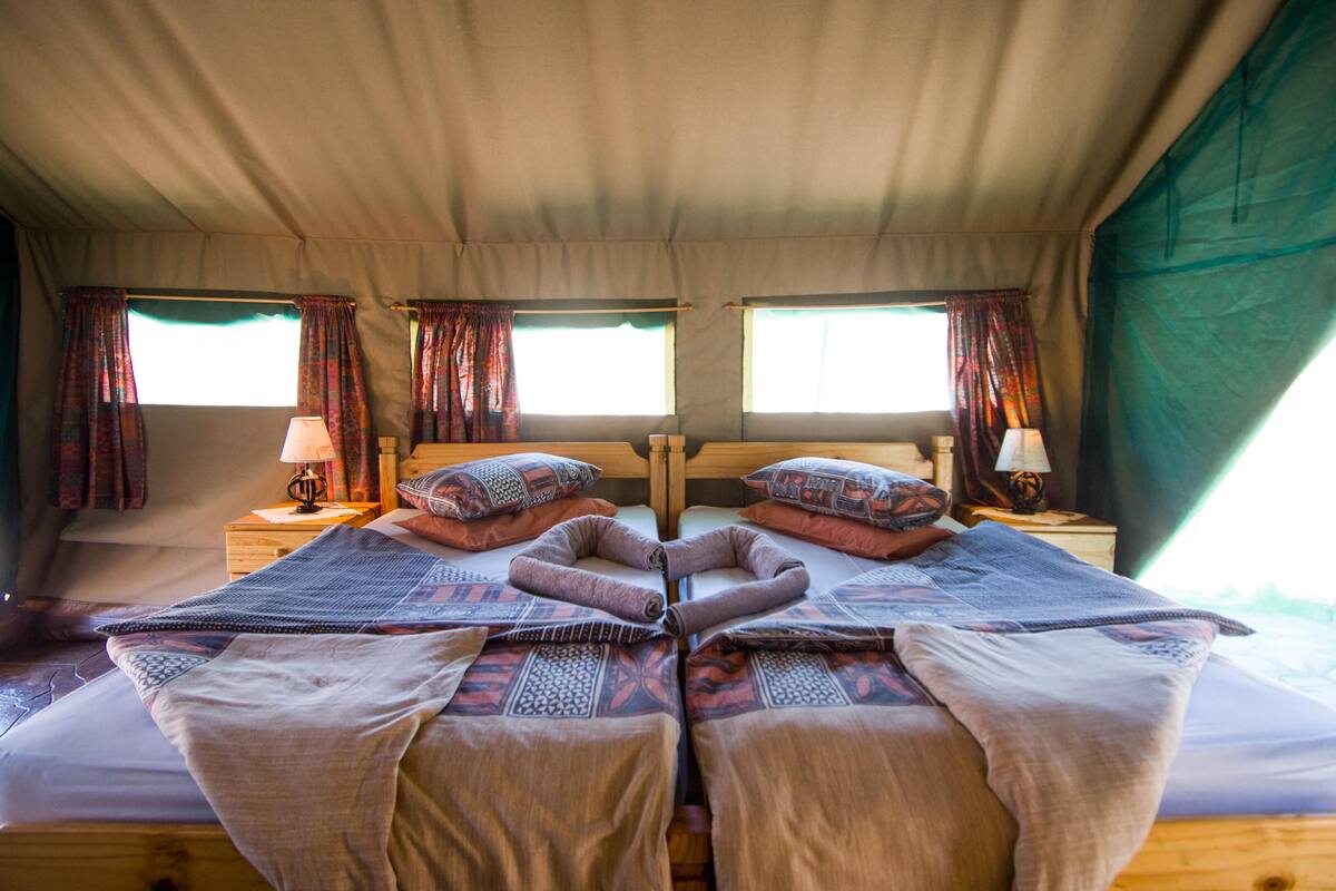 A cozy, well-lit tent-style room with two beds, each with patterned bedding and pillows, and two bedside tables with lamps.