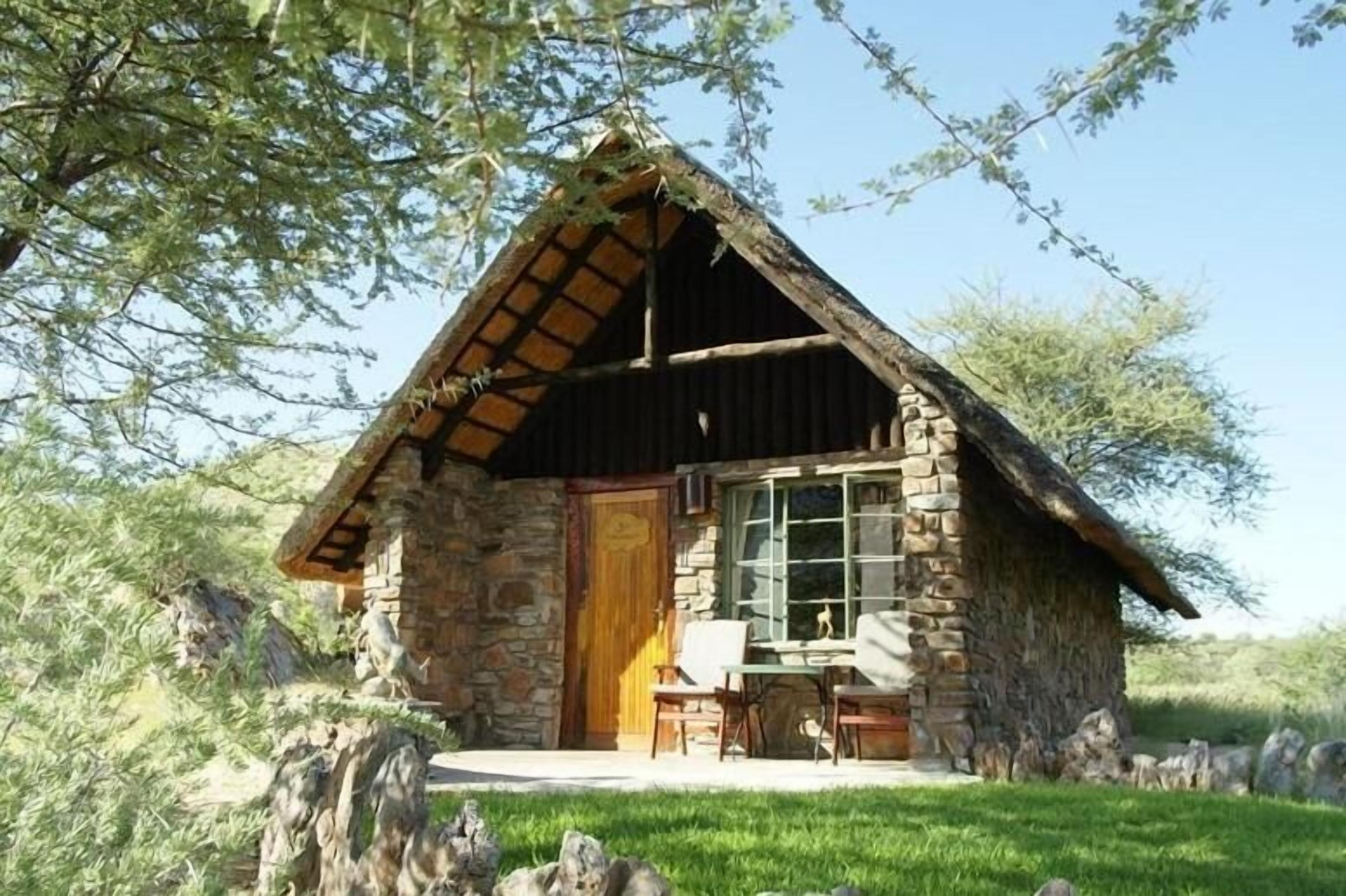 Eine Steinhütte mit Holztür, einem Fenster und einer kleinen Veranda mit Tisch und Stühlen.