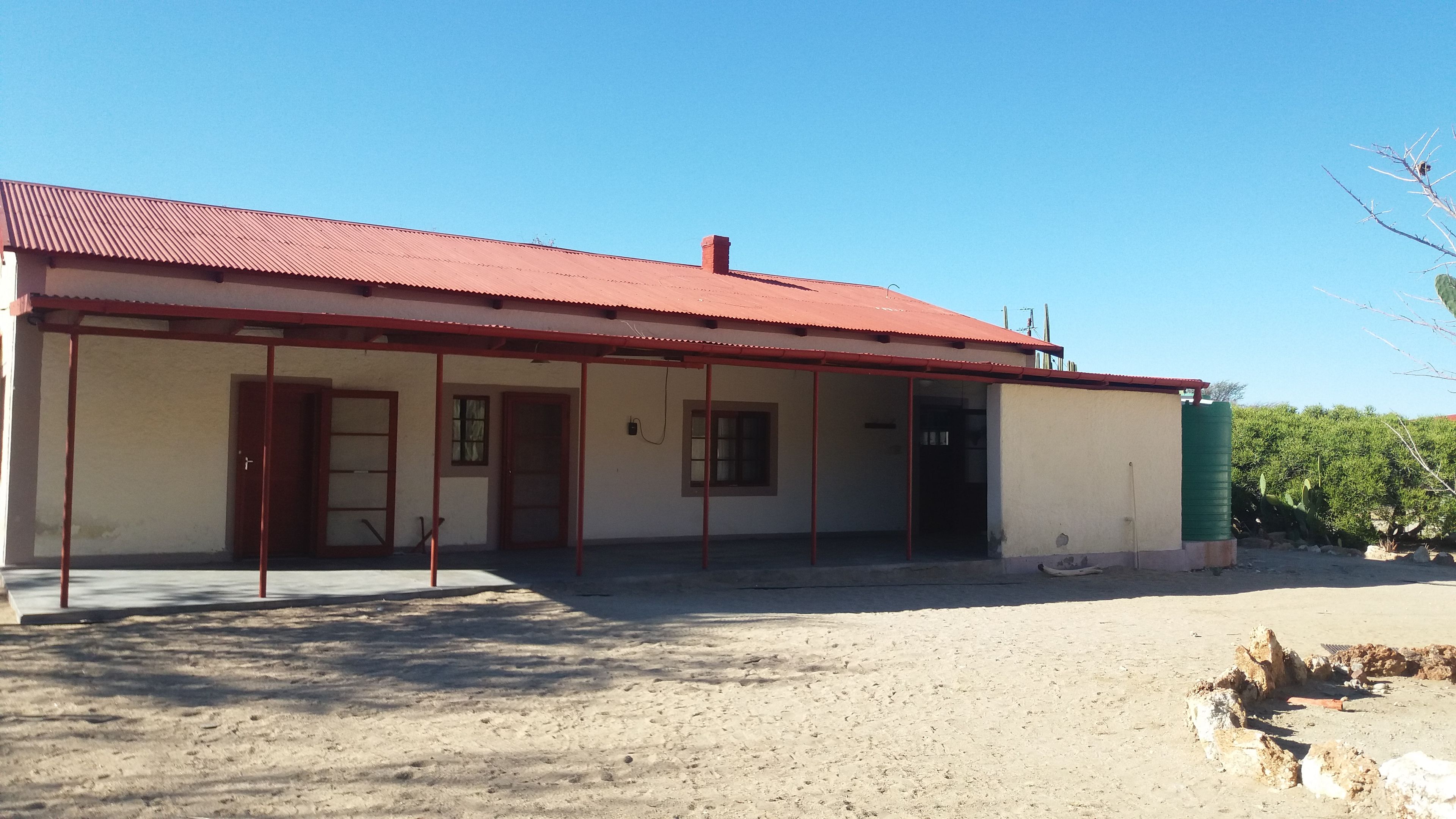 A single-story building with a red roof, a covered porch, and a small water tank.