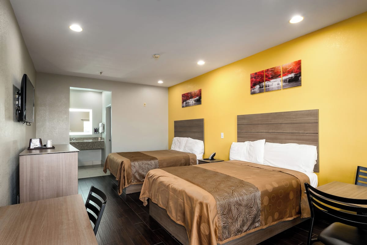 Quarto de hotel com duas camas, uma escrivaninha e uma cadeira. É visível um banheiro ao fundo.