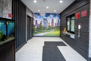 A modern hotel lobby with a cityscape mural, a reception desk, and a reception area. - Moonlight Suites - Houston George Bush Intl Airport (Houston)