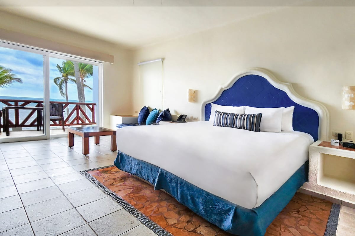 Habitación de hotel con una cama grande, un escritorio y vistas a las palmeras y al océano.