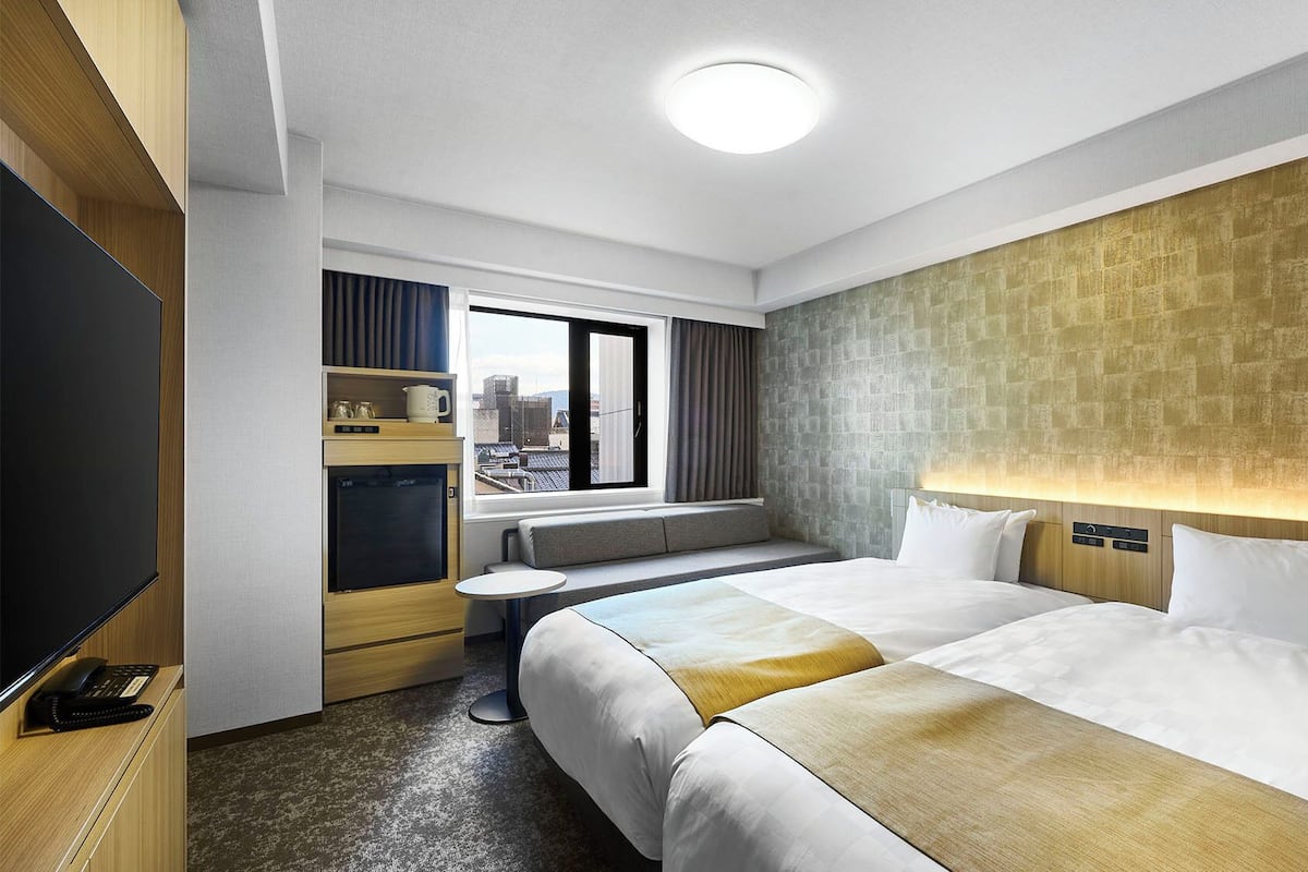Une chambre d’hôtel avec un lit, un bureau, une télévision, une fenêtre et une vue sur la ville.