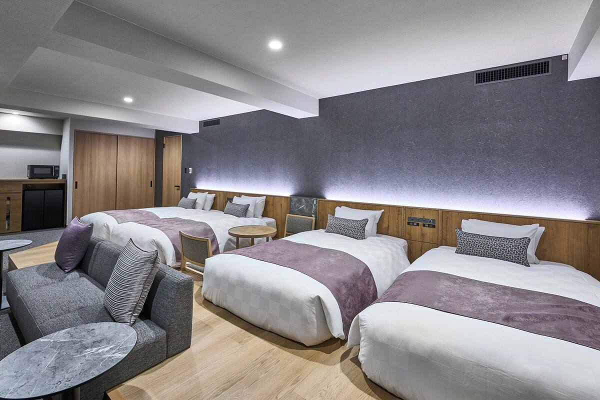 Une chambre d’hôtel avec trois lits, un canapé, une petite table et un four à micro-ondes.