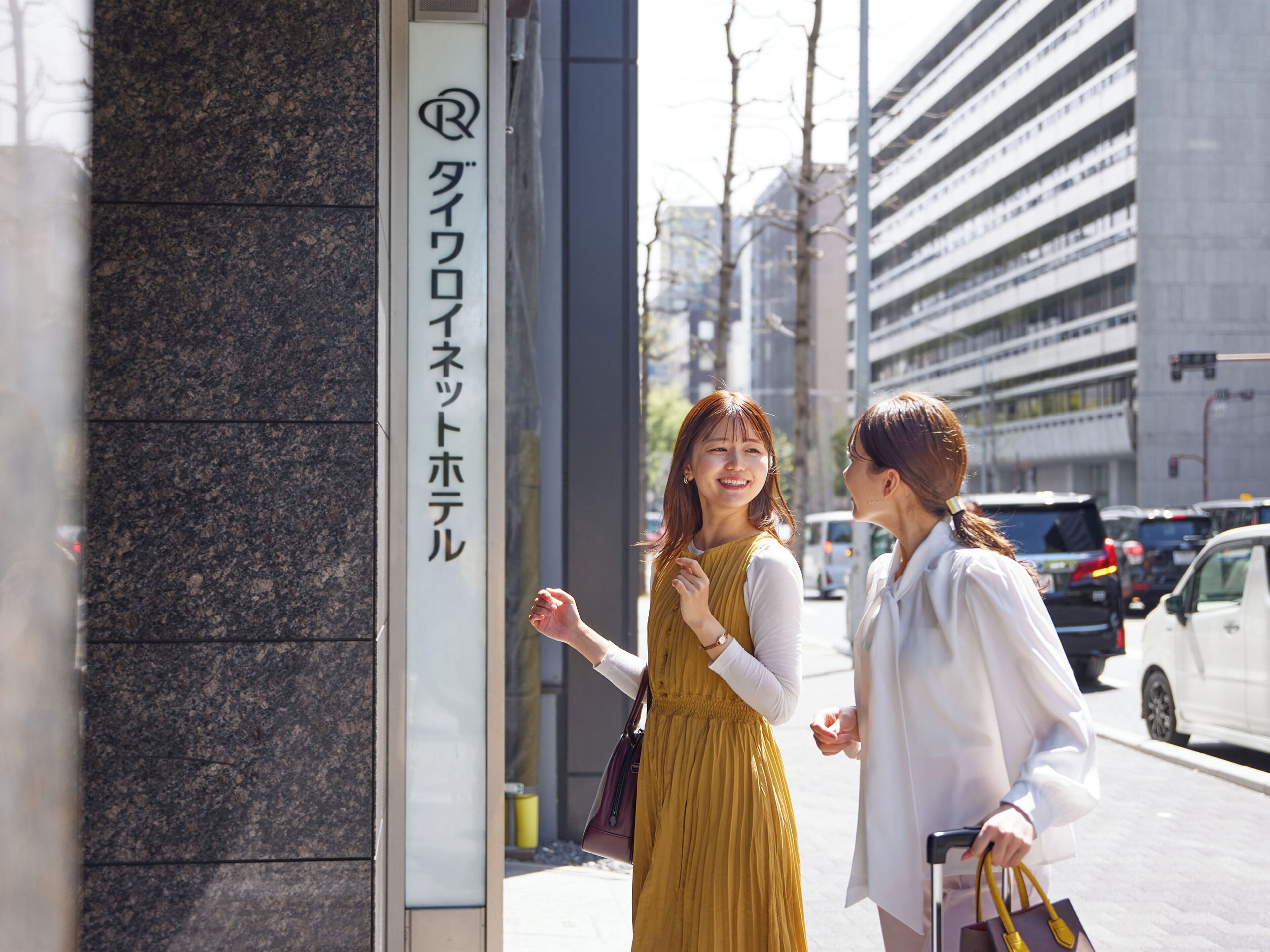 Two people standing in front of a building with a sign that includes Japanese characters.