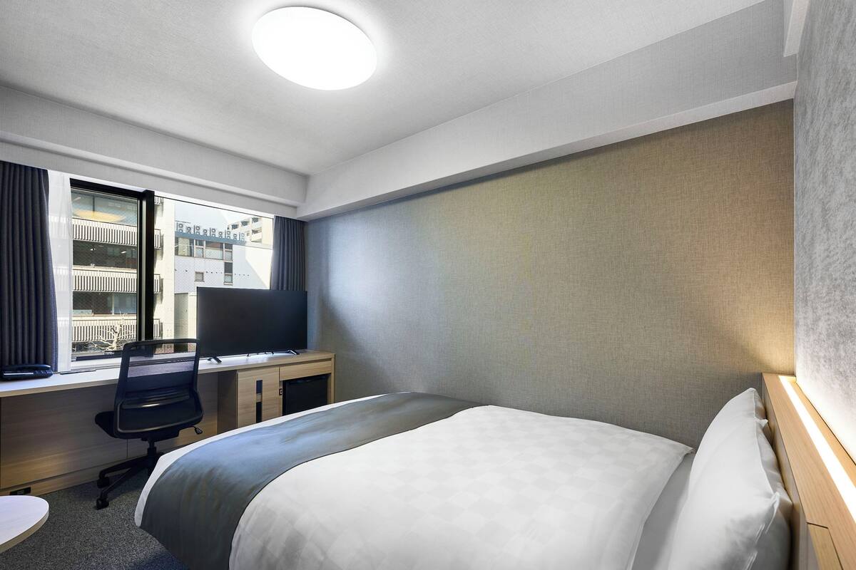 Une chambre d’hôtel équipée d’un lit, d’un bureau, d’une chaise, d’une télévision et d’une fenêtre avec des rideaux.