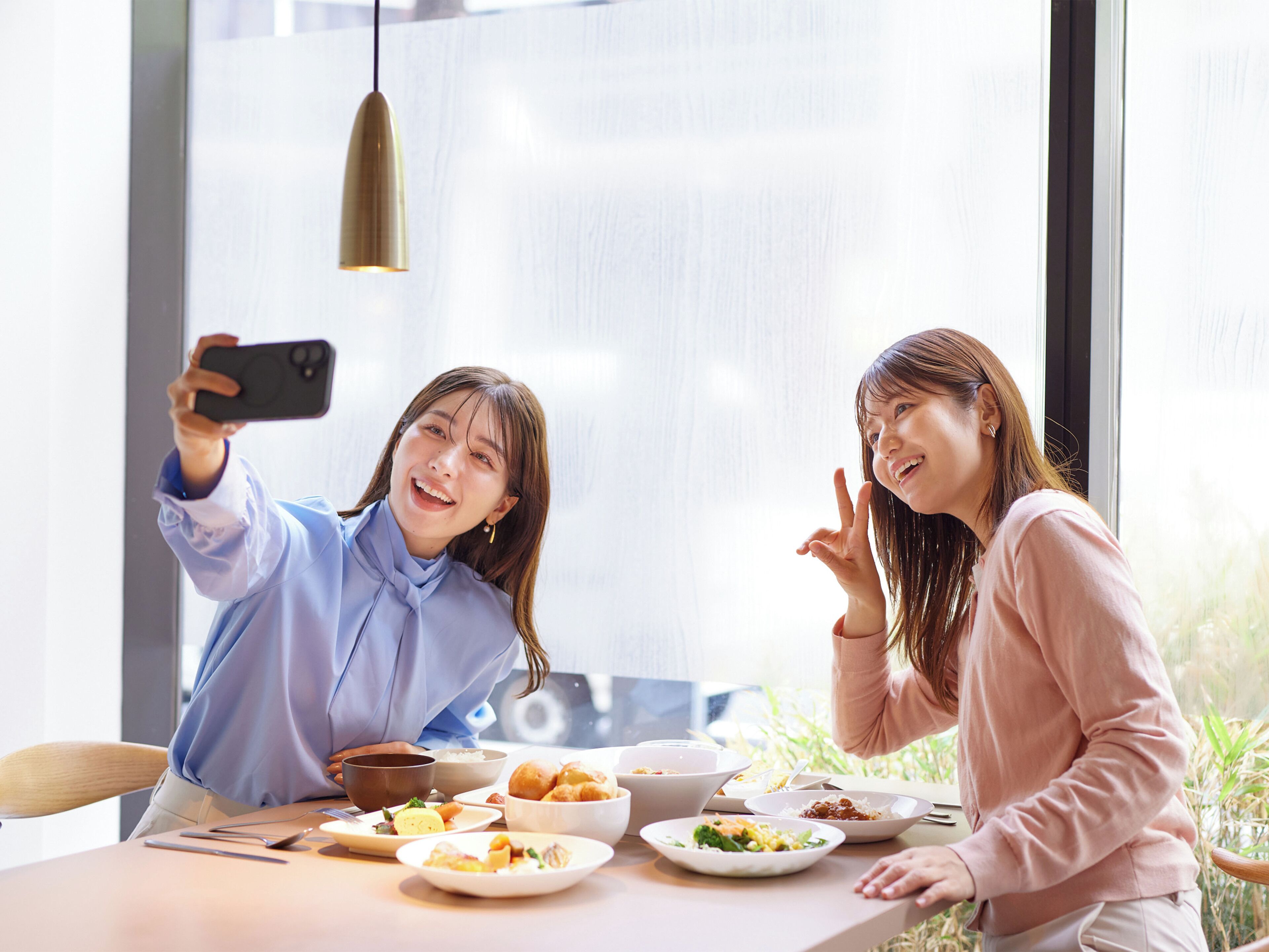 Dos personas sentadas en una mesa con varios platos, tomándose un selfie.