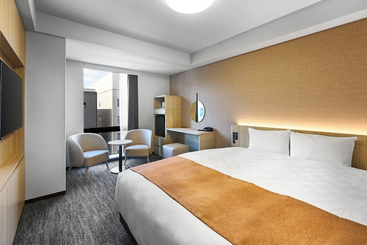 Une chambre d’hôtel moderne équipée d’un grand lit, d’un bureau, d’une chaise, d’une petite table et d’un téléviseur.