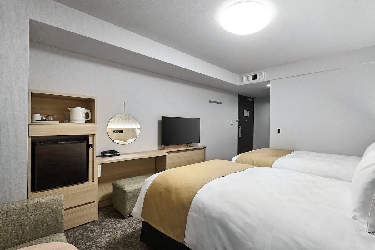 Une chambre d’hôtel avec deux lits, une télévision, une machine à café et un miroir.