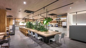 A modern interior with a long communal table surrounded by chairs, a kitchen area, and a seating area with sofas.