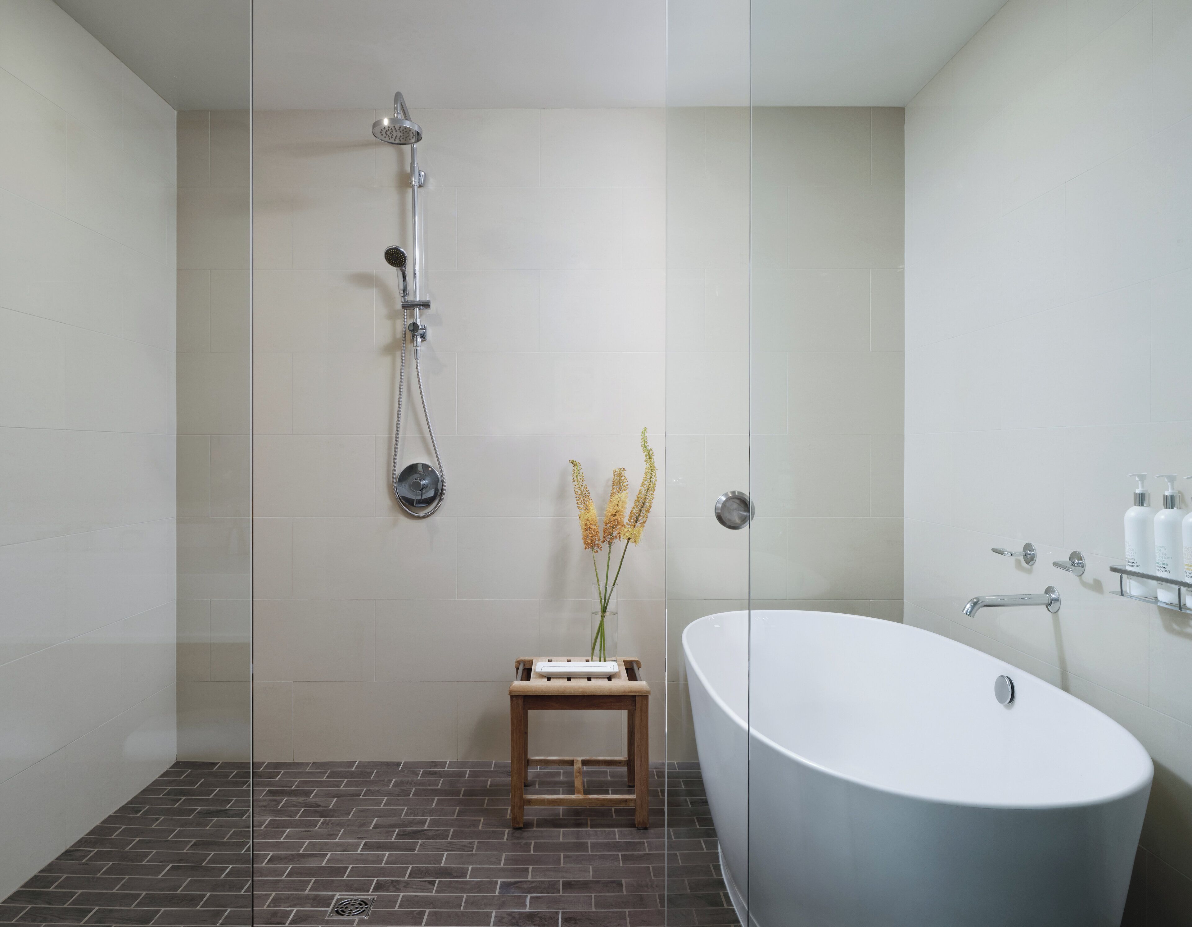 A modern bathroom with a freestanding bathtub, a glass-enclosed shower, and a small wooden stool.