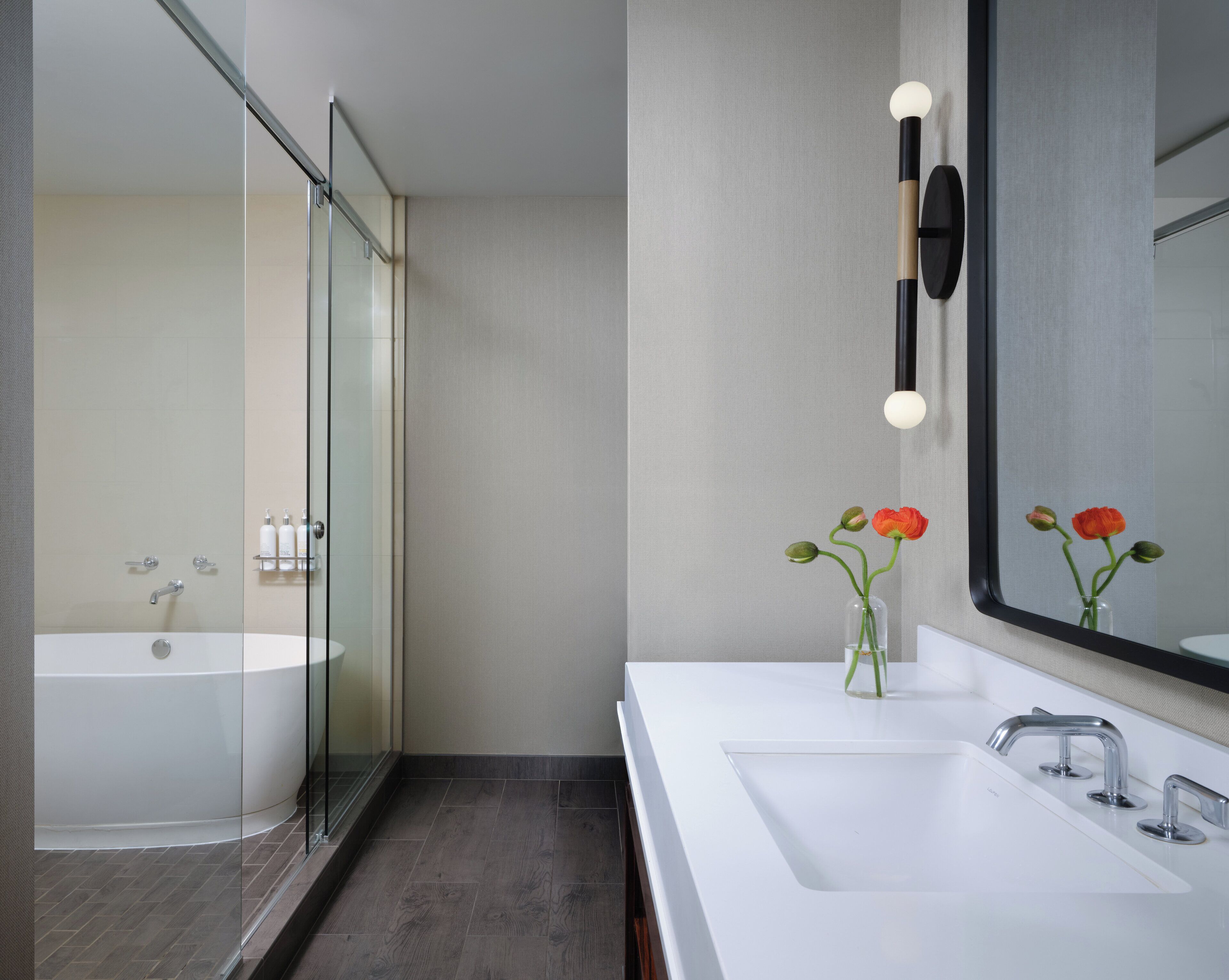 Un baño moderno con cabina de ducha de vidrio, un lavabo blanco con espejo y un jarrón con flores.