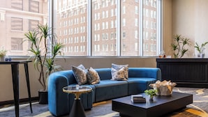 A modern living room with a blue sofa, a round coffee table, and two potted plants. - Kimpton Hotel Palomar Phoenix Cityscape by IHG (Phoenix)