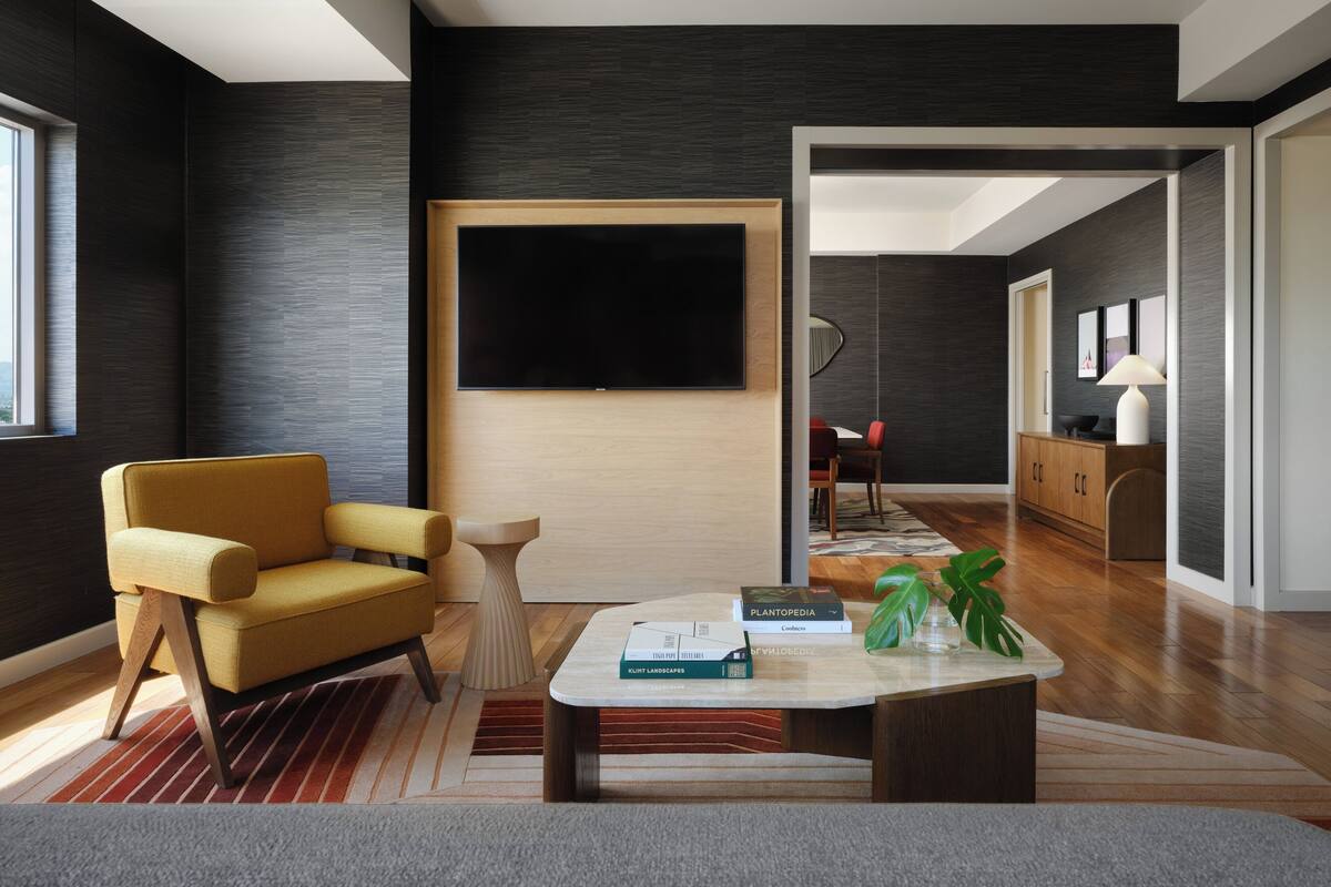 A modern living room with a sofa, coffee table, and books. A flat-screen TV is mounted on the wall.