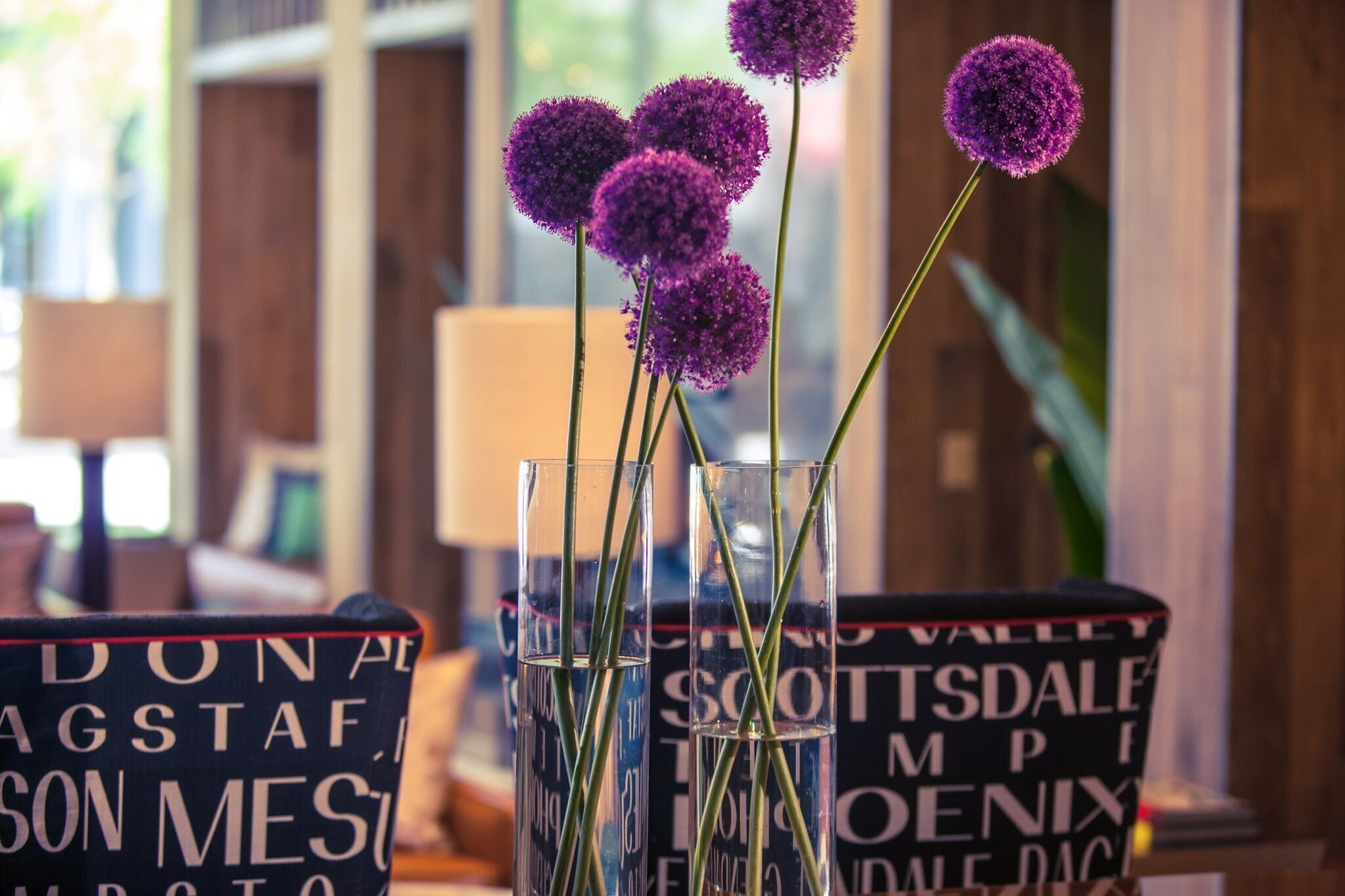 Una mesa con jarrones que contienen flores moradas y libros con títulos visibles.