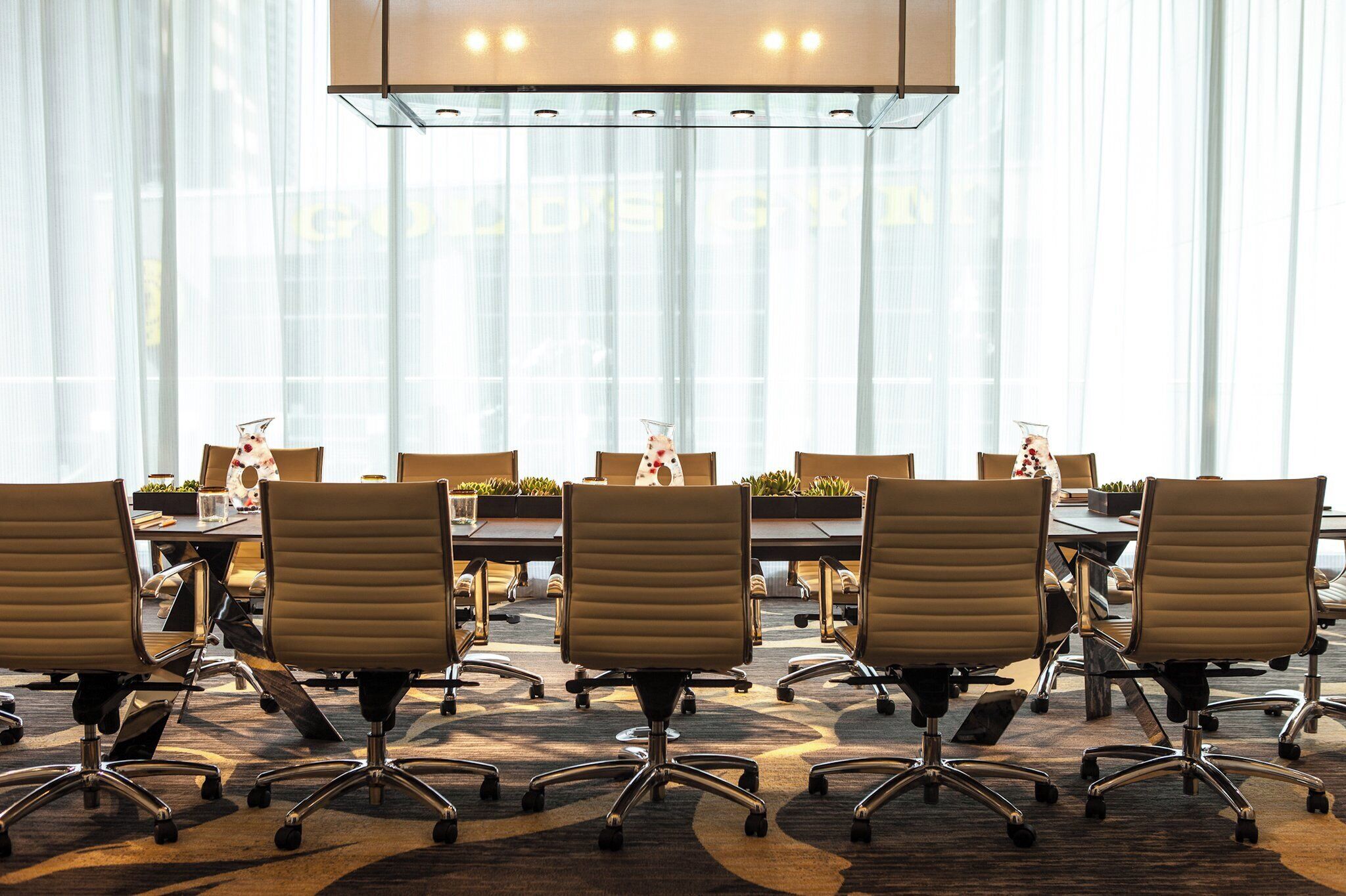 A conference room with a long table, multiple chairs, and a modern ceiling light fixture.