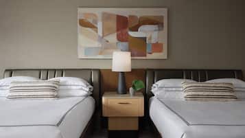 Una habitación de hotel con dos camas, una mesita de noche con lámpara, una planta pequeña y una obra de arte abstracta en la pared.