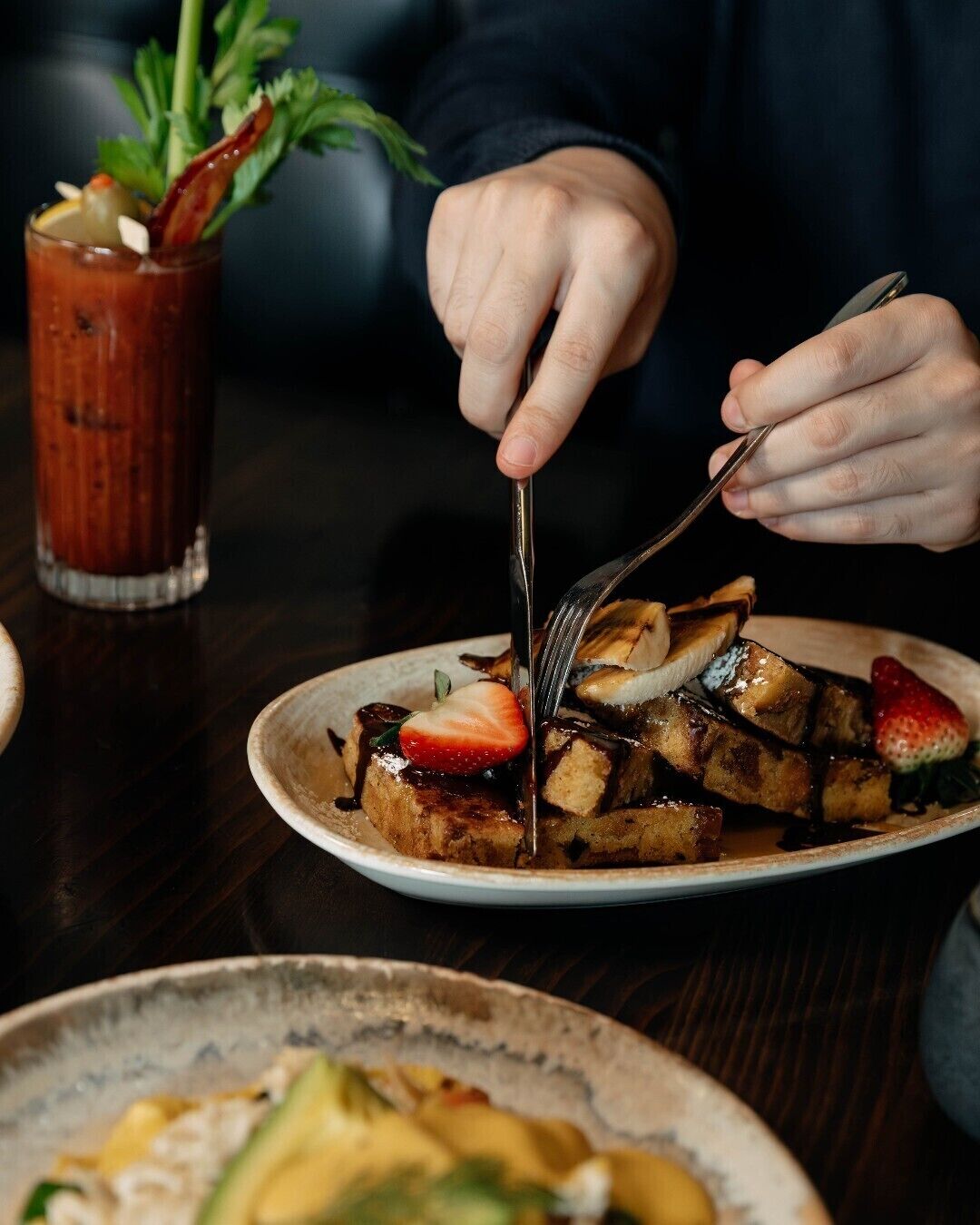 Une personne qui découpe une assiette contenant un steak, des toasts et des fraises.