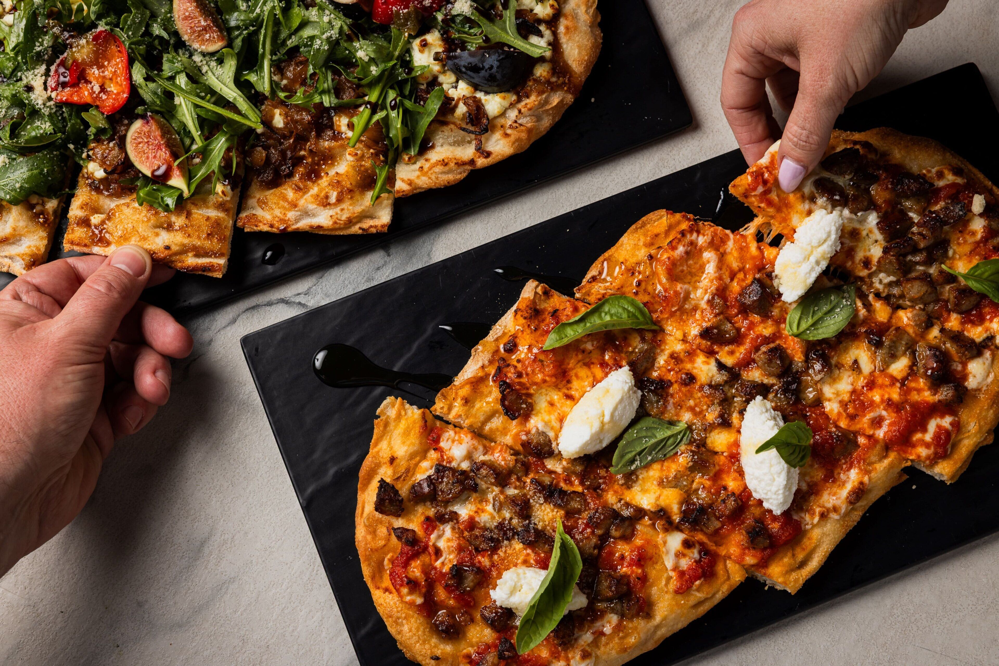 Deux pizzas sur une assiette en ardoise noire, avec un couteau.
