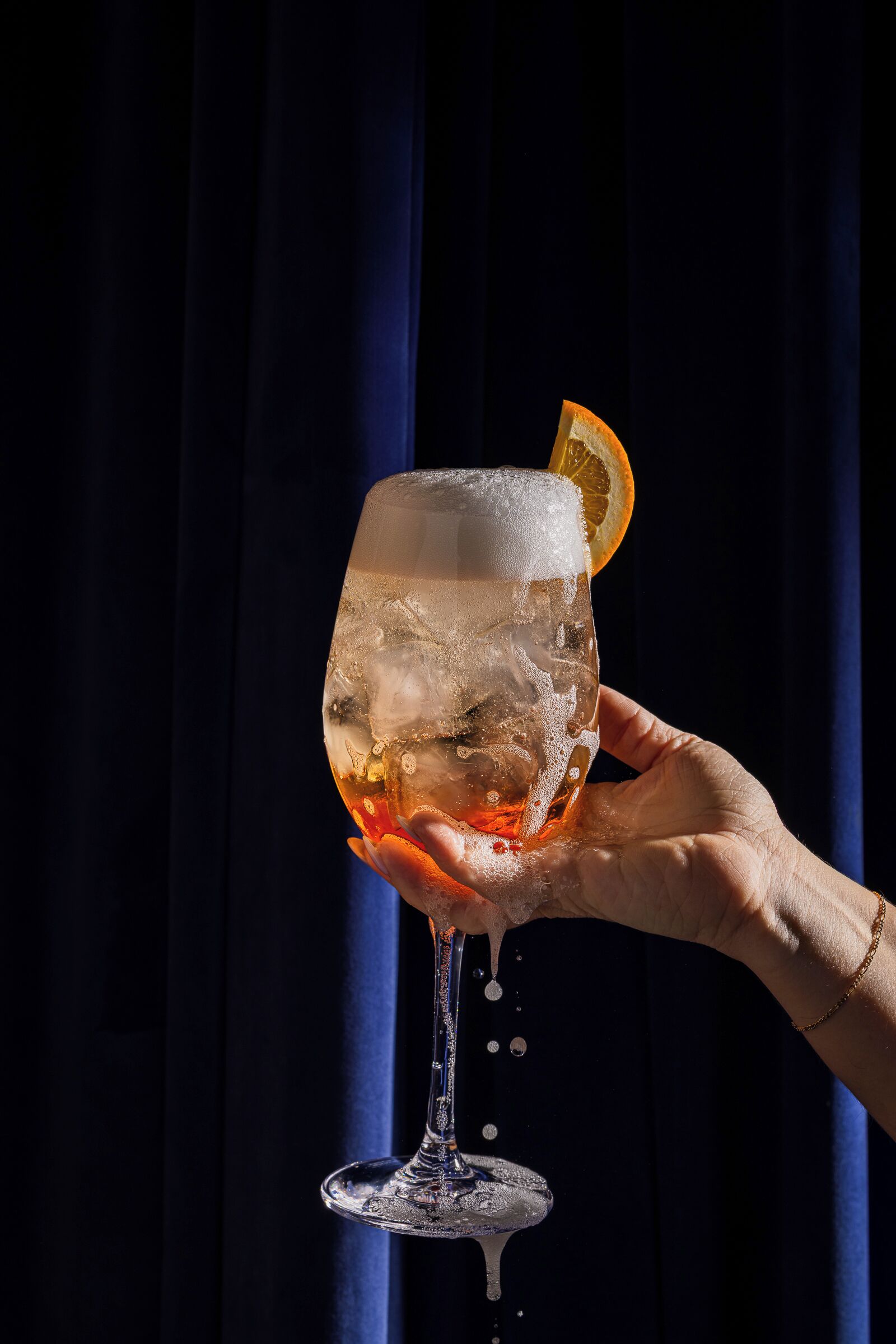 Una mano sosteniendo un vaso con hielo y una rodaja de naranja.