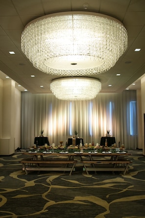 A banquet hall with a large chandelier, a long table set for a meal, and a backdrop of curtains.
